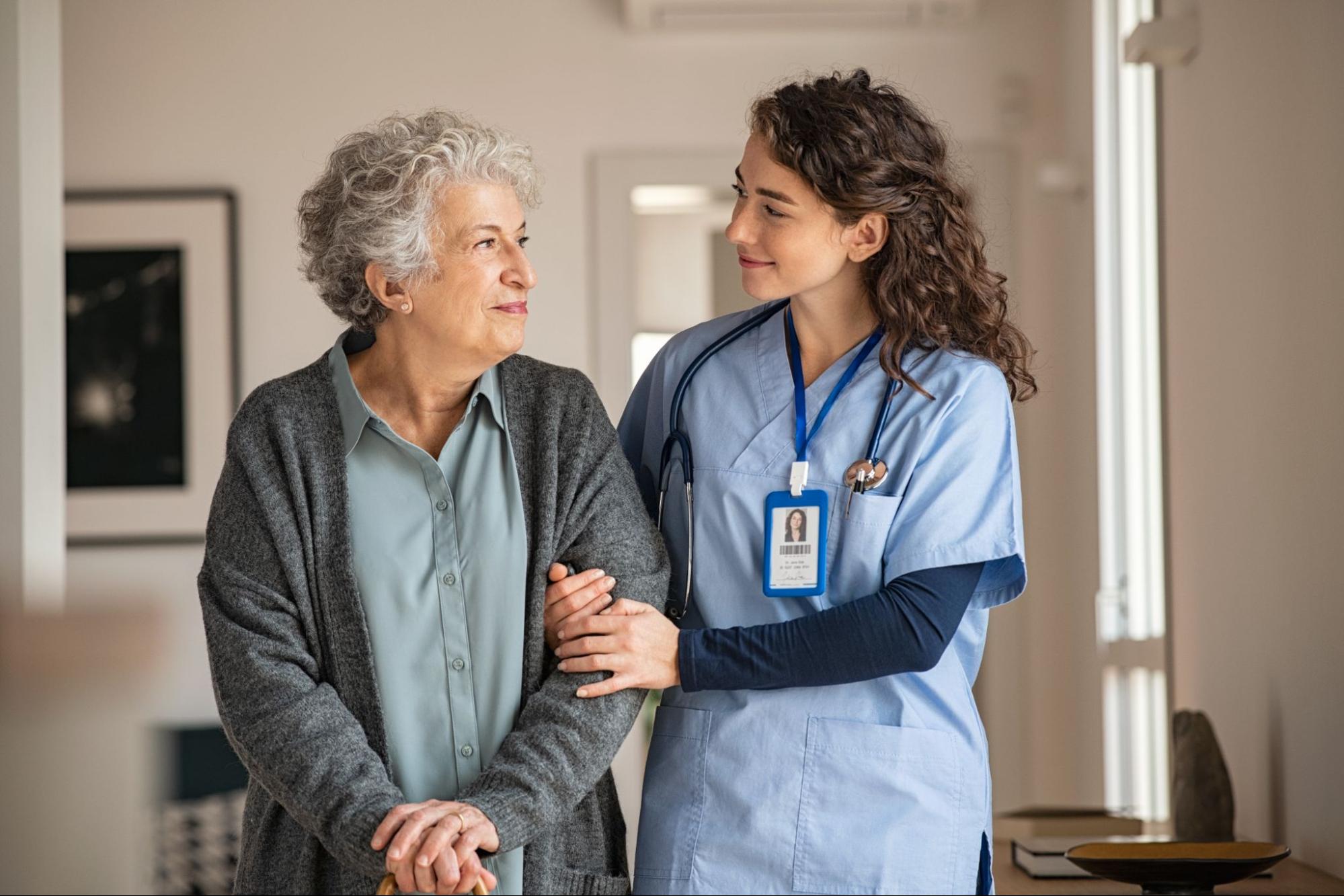 Nurse gently supporting an elderly woman with a warm smile.