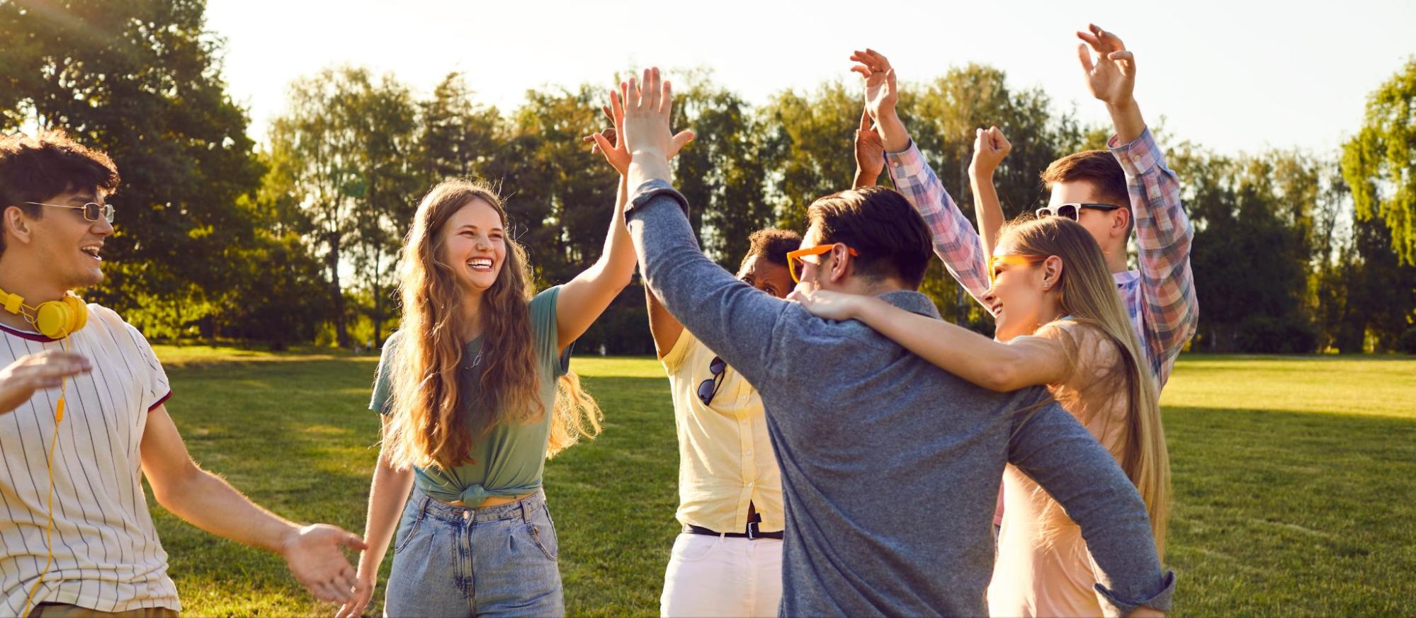 Group of young adults smiling and high-fiving in a park.