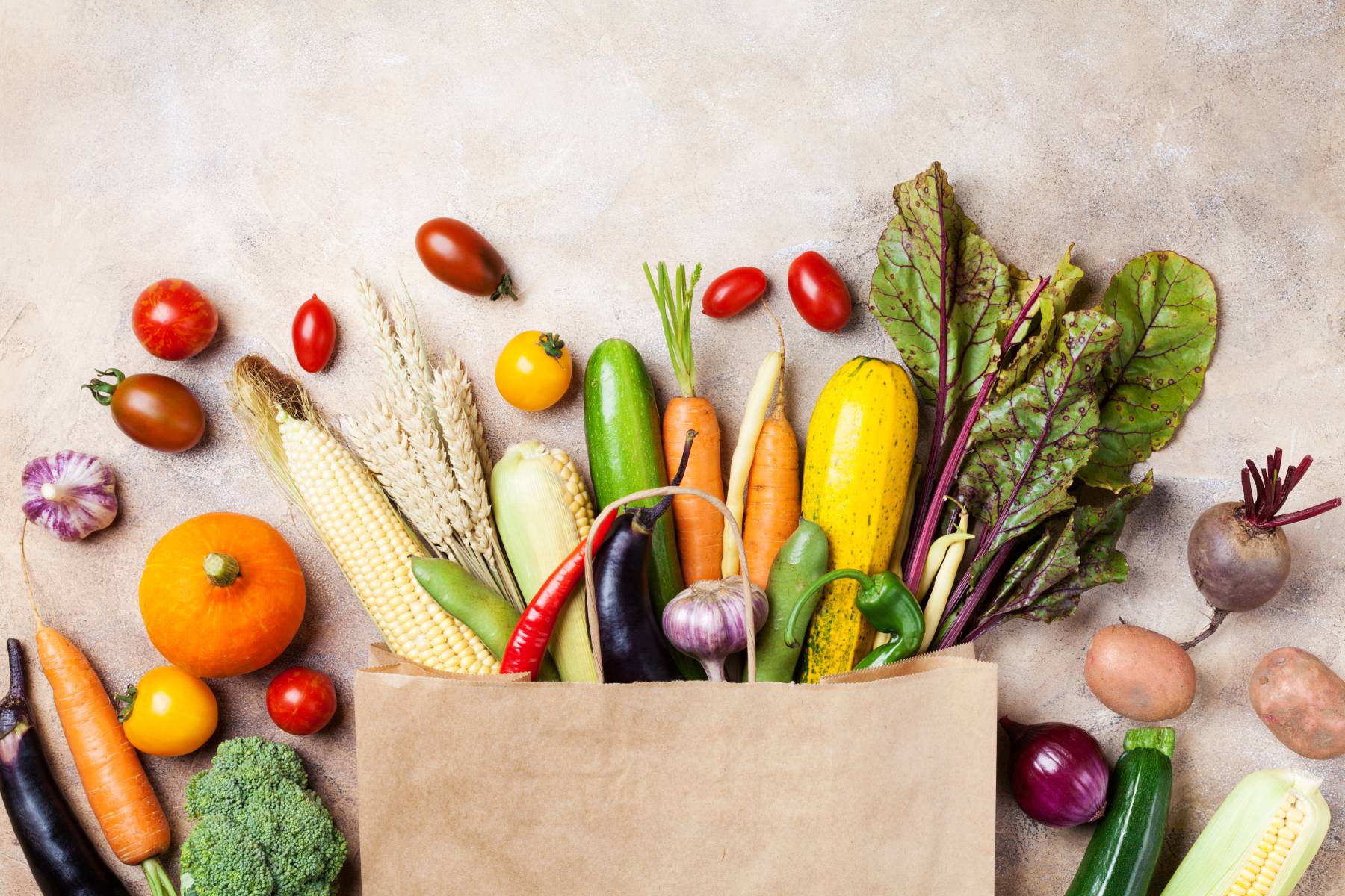 Grocery bag filled with fresh fall produce, including squash, carrots, apples, and leafy greens