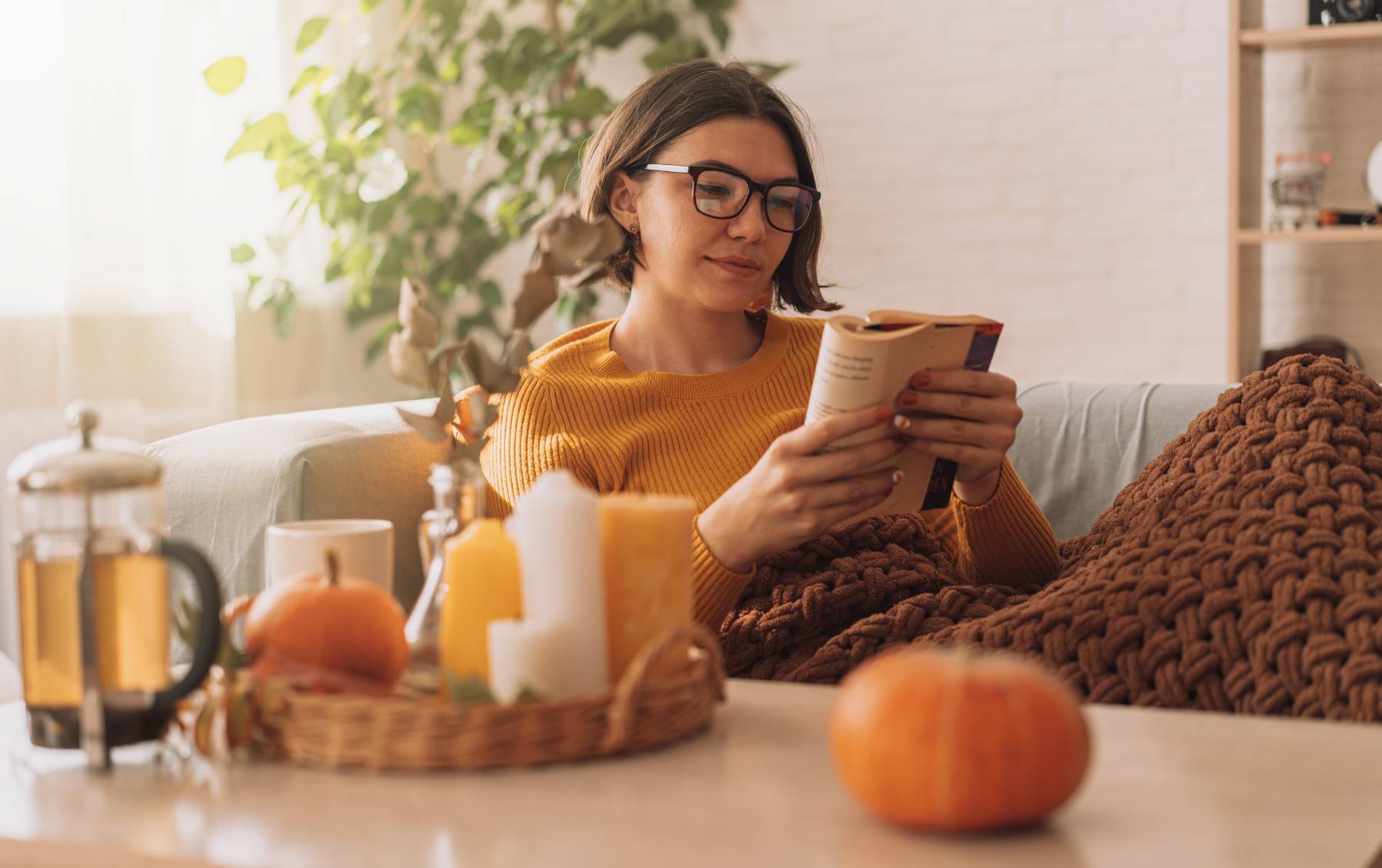 Woman enjoying tea at home surrounded by cozy fall decorations.