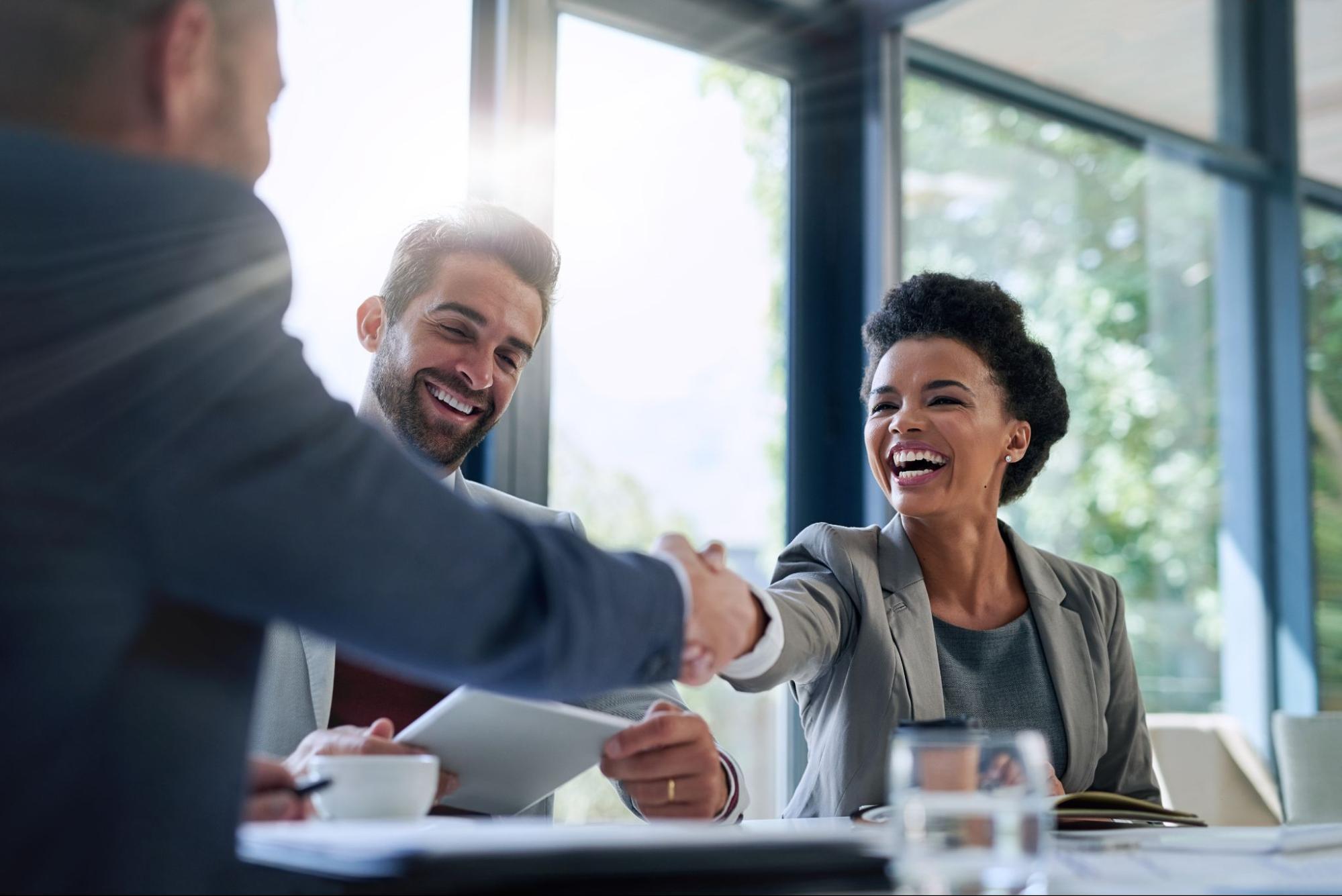 Two business professionals smile and shake hands during a successful meeting in a bright office setting.