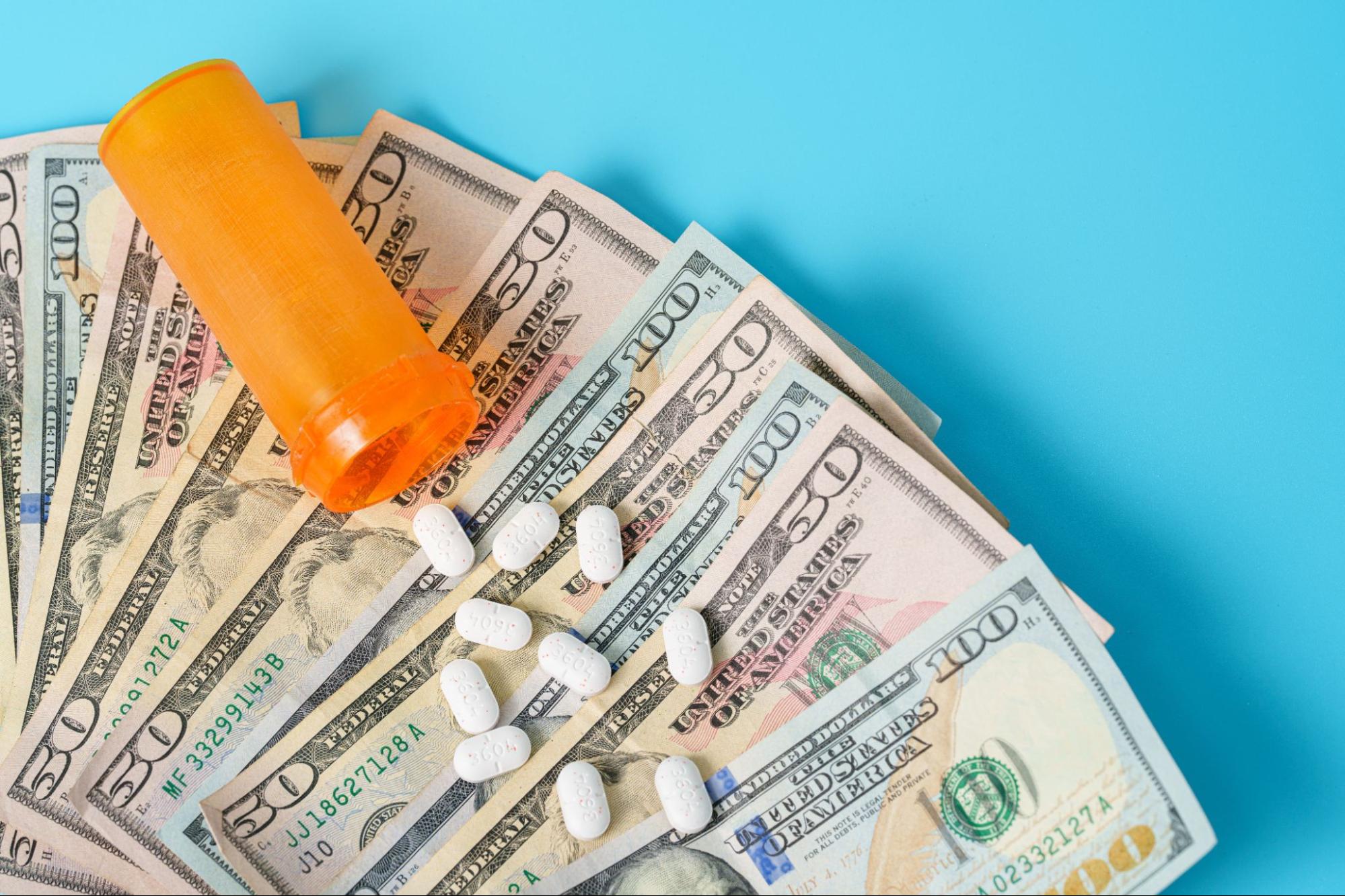 Prescription pills and bottle on a stack of money, symbolizing high heatlhcare costs in America.